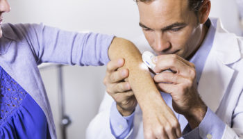 Dermatologist examining mole with dermatoscope, professional clinic setting